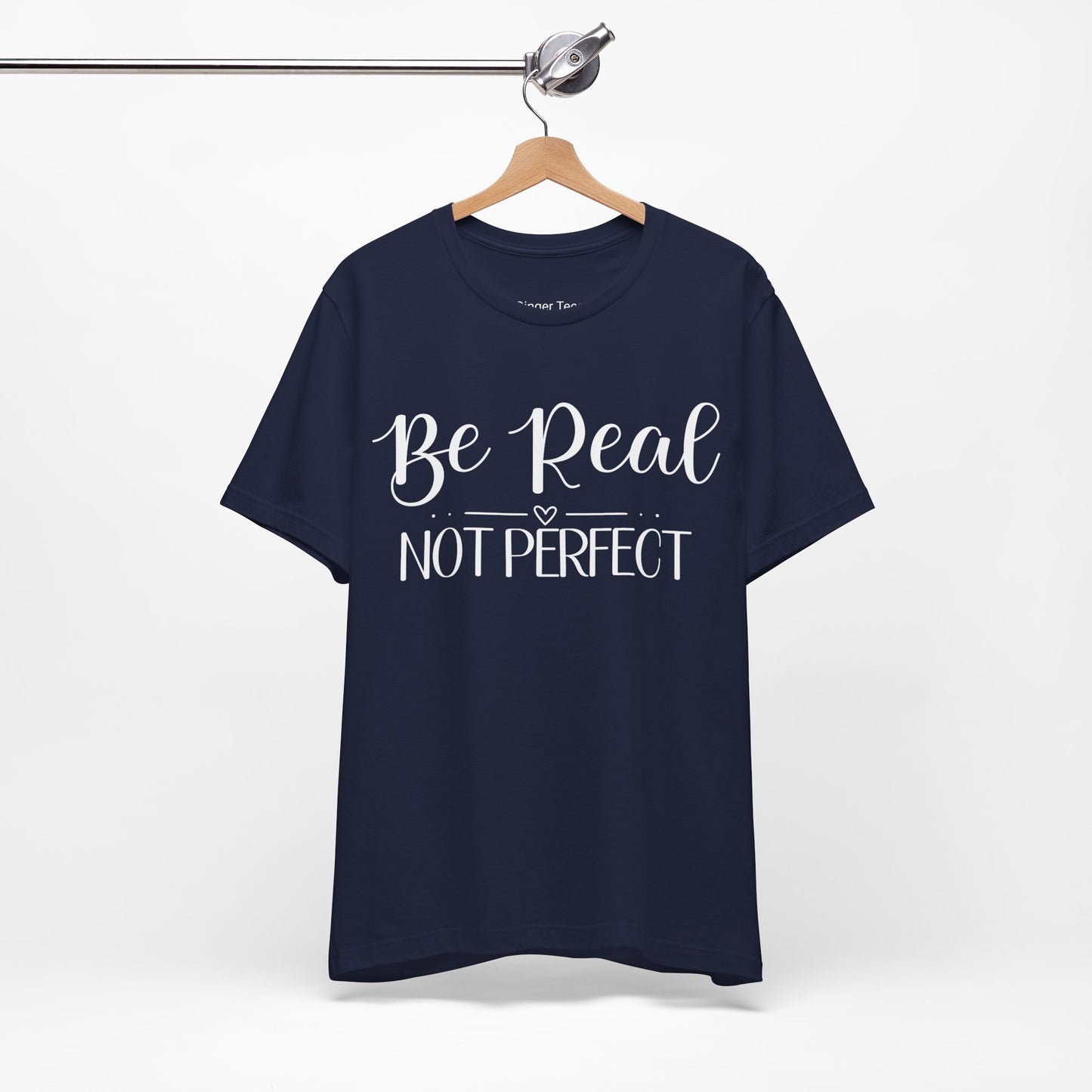 Be Real Not Perfect" t-shirt in natural, navy, and soft pink. Features a bold white script font with a heart accent, promoting authenticity and self-acceptance.