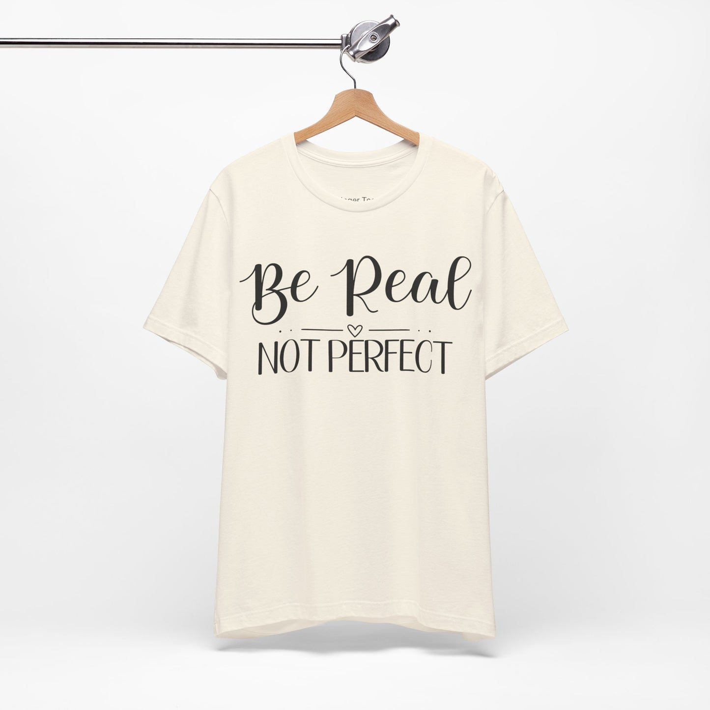 Be Real Not Perfect" t-shirt in natural, navy, and soft pink. Features a bold white script font with a heart accent, promoting authenticity and self-acceptance.