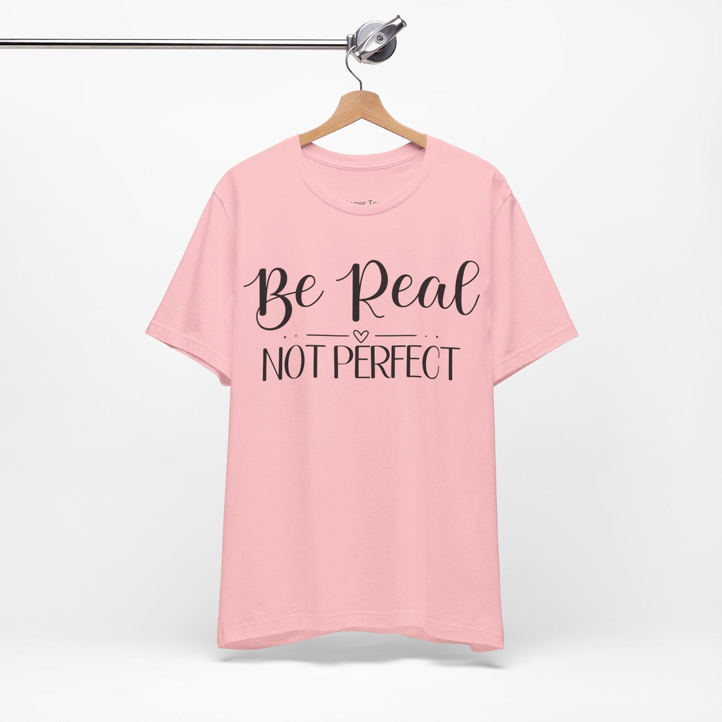 Be Real Not Perfect" t-shirt in natural, navy, and soft pink. Features a bold white script font with a heart accent, promoting authenticity and self-acceptance.