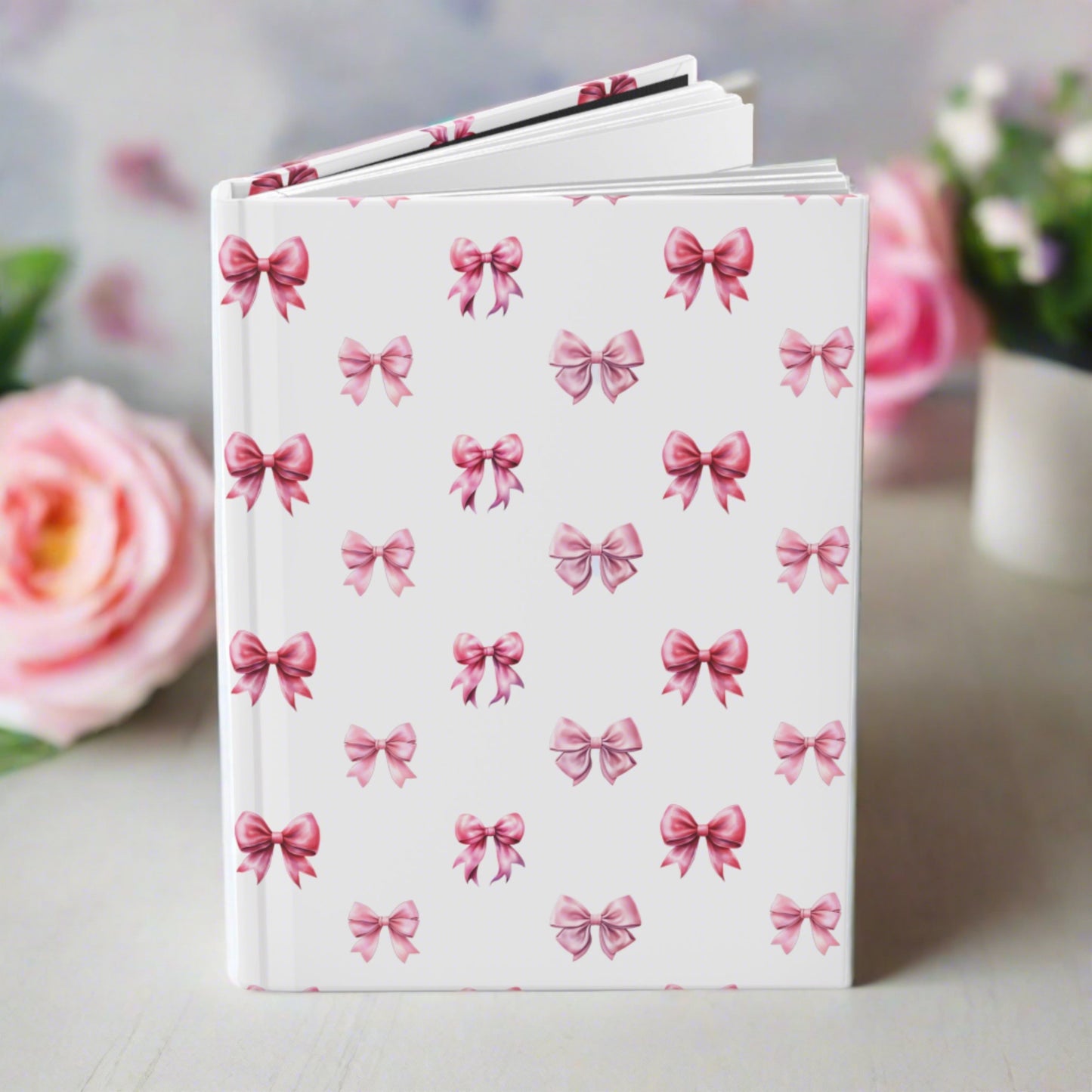 coquette pink bow pattern on a hardcover journal. on a desk with pretty roses