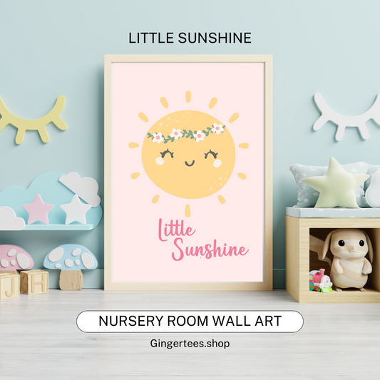Framed nursery wall art print featuring a cheerful yellow sun with closed eyes, rosy cheeks, and a floral crown, smiling above the words “Little Sunshine” in pink script on a soft pastel pink background. Displayed in a cozy nursery room with pastel decor and plush toys.